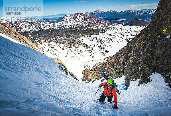 Mann mit Splitboard auf dem Rücken erklimmt steile Schneerinne