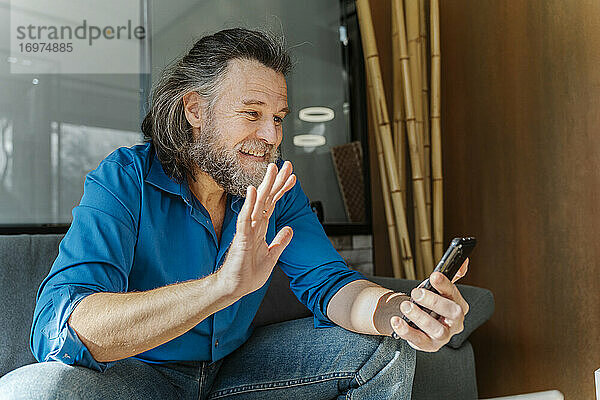 Älterer Mann mit Bart sitzt auf einem Sofa und schaut auf sein Smartphone