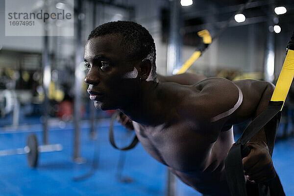 Afroamerikanischer Mann trainiert mit TRX-Geräten im Fitnessstudio