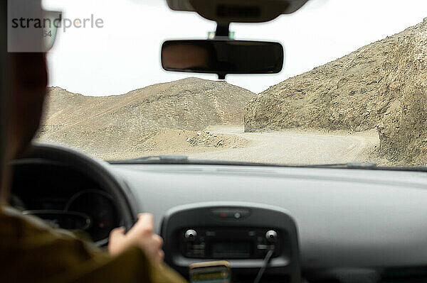 Mann am Steuer eines Autos auf einer Bergstraße in der Wüste. Autoreise.