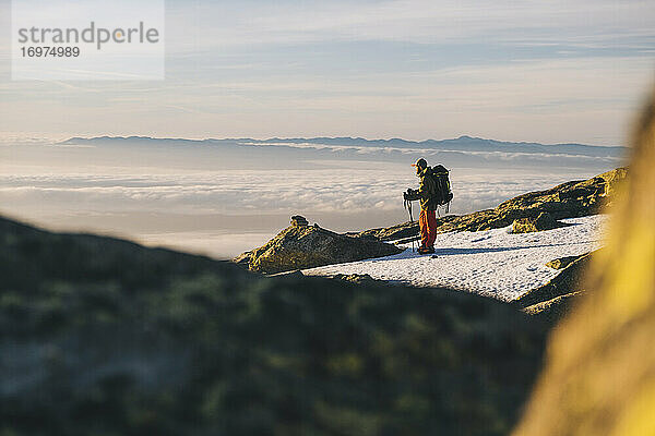 Junger Mann mit Mütze und Blick auf die über dem Horizont aufgehende Sonne  gegen die Wolken  Gredos  Spanien