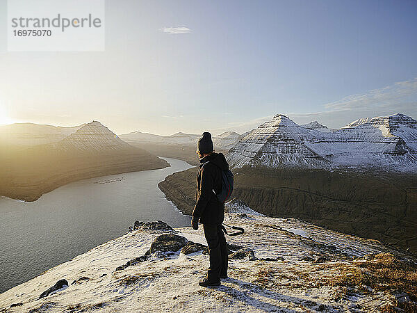 Frau auf verschneitem Berg mit Blick auf das Meer auf den Färöer Inseln