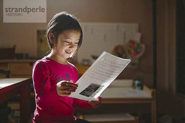 Ein lächelndes Kind in schönem Licht studiert ein Blatt Papier und liest