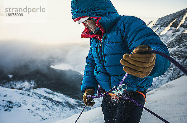 Männlicher Kletterer sichert seinen Vorsteiger bei einer kalten alpinen Wintertour