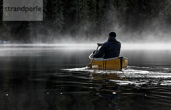 Bärtiger Abenteurer paddelt allein auf einem ruhigen  nebligen See im Kanu