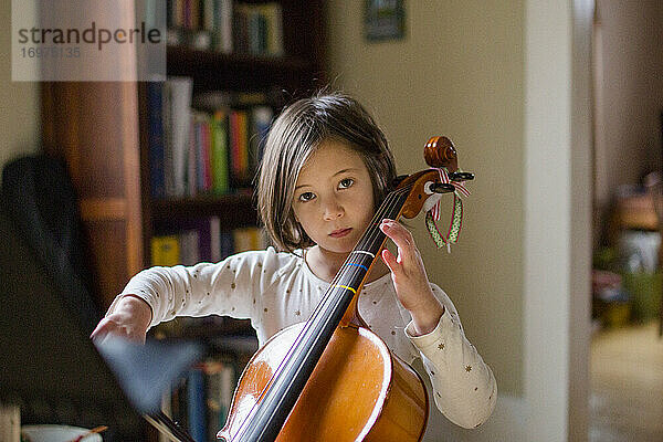 Ein ernsthaftes kleines Mädchen übt zu Hause bei schönem Licht Cello