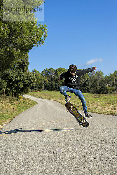 Action Shot eines jungen Skater Teenager männlich springen hoch auf einem Hügel Straße