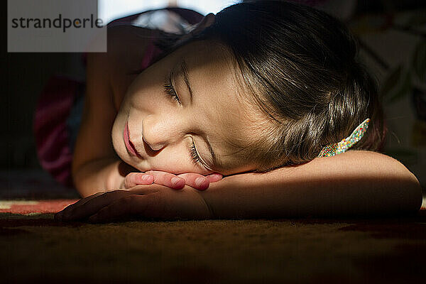 Ein kleines Mädchen liegt mit geschlossenen Augen in einem hellen Lichtfleck und lächelt