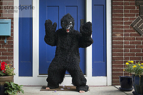 Ein Junge mit Gorillakostüm und Maske steht barfuß auf der Treppe vor dem Haus