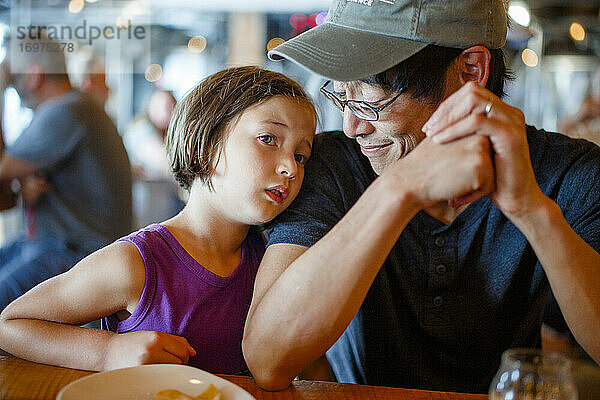 Ein Vater lächelt auf sein Kind herab  das sich in einem überfüllten Restaurant an ihn lehnt