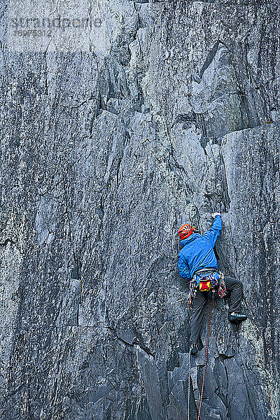 Mann klettert in einem Schiefersteinbruch in Nordwales eine steile Felswand hinauf