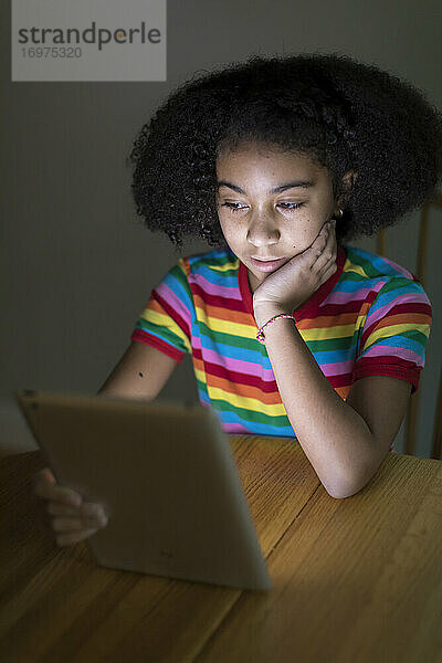 zehnjähriges gemischtrassiges Mädchen  das am Tisch auf ein iPad schaut