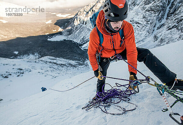 Ein männlicher Kletterer sichert einen anderen Kletterer während einer alpinen Eiskletterei im Winter