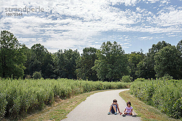 Zwei kleine Kinder sitzen zusammen auf einem Weg durch eine Wiese in einem Park