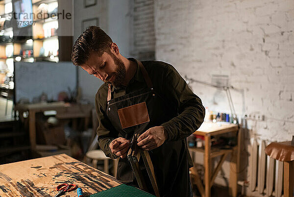 Bärtiger Handwerker beim Zusammenbau der Ausrüstung in einer Lederwerkstatt