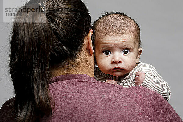 Neugeborenes Baby schaut über die Schulter seiner Mutter und starrt mit großen Augen