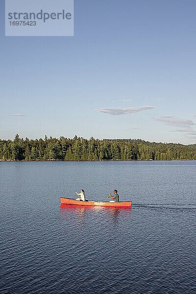 Mehrrassiges Paar paddelt mit rotem Kanu auf einem See in der Wildnis in den Wäldern von Maine