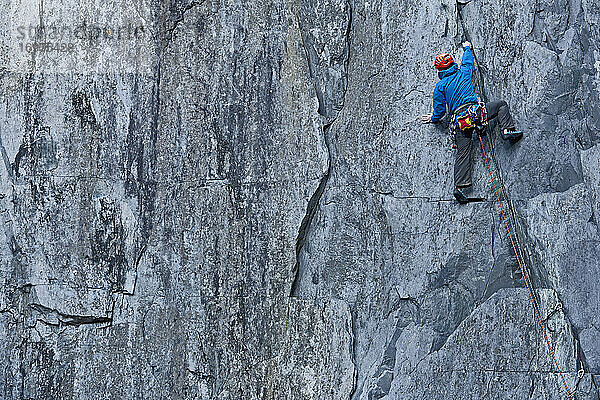 Mann klettert in einem Schiefersteinbruch in Nordwales eine steile Felswand hinauf