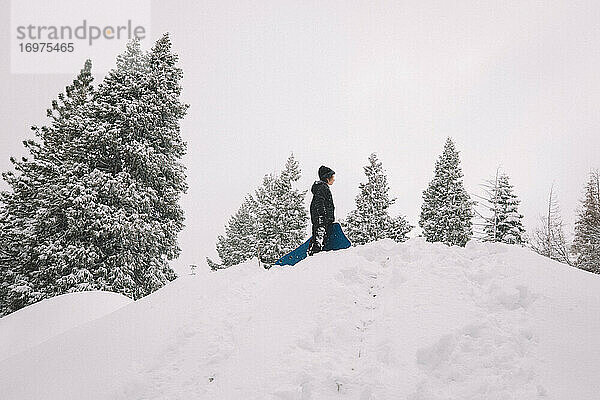 Junge steht mit Schlitten auf einem verschneiten Hügel