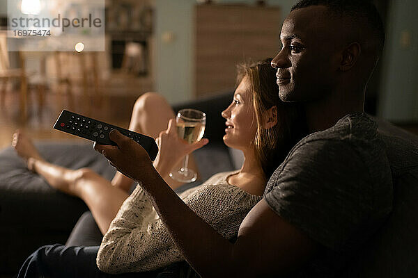 Multiethnisches Paar mit Weinglas vor dem Fernseher