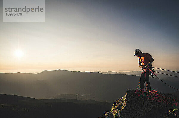 Mann beim Sichern mit Kletterseilen bei Sonnenaufgang in den Bergen