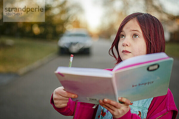 Ein kleines Mädchen mit Notizbuch und Bleistift blickt auf und beobachtet die Natur