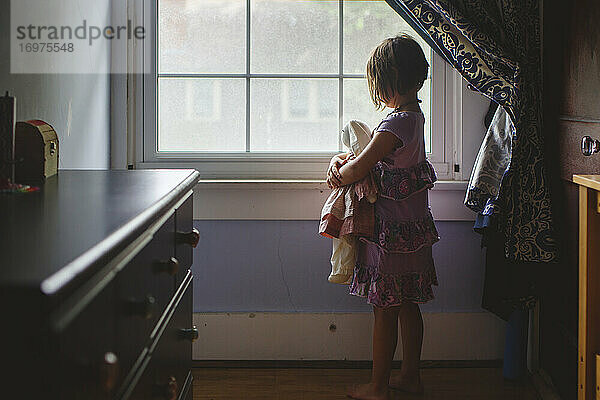 Porträt eines kleinen Kindes  das allein im Schlafzimmer steht und ein Stofftier hält