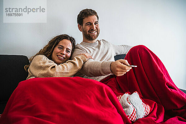 Fröhlicher Mann und Frau sehen auf einer Decke fern