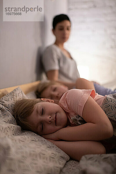 Mädchen schläft auf dem Bett neben Schwester und Mutter