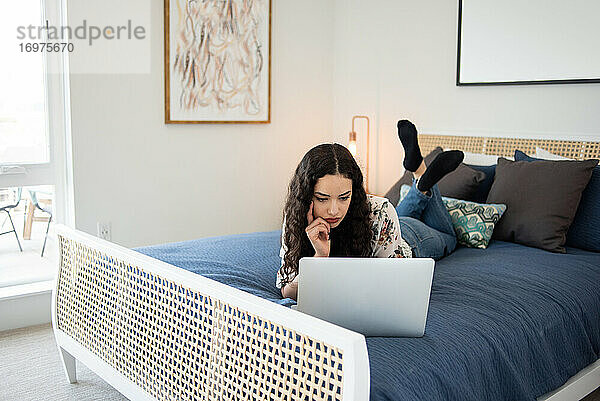 Junge Frau liegt auf dem Bett und schaut auf einen Laptop