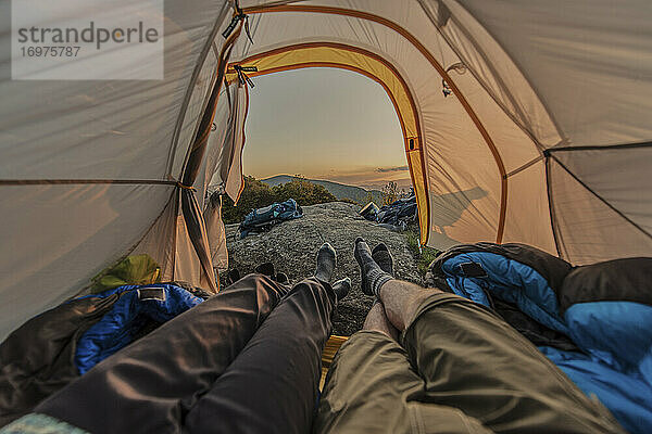 POV-Aufnahme von zwei Menschen  die im Zelt liegen und in den Sonnenuntergang blicken