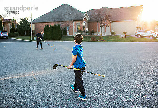 Zwei Jungen spielen Streethockey in einer Wohnstraße im Herbst.