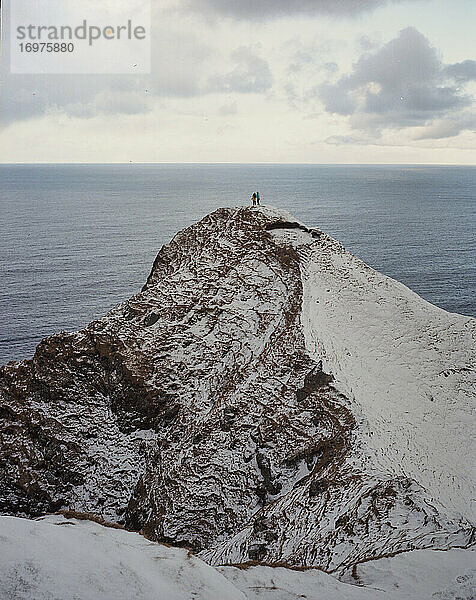 Zwei Menschen stehen am Rande einer verschneiten Klippe auf den Färöer-Inseln