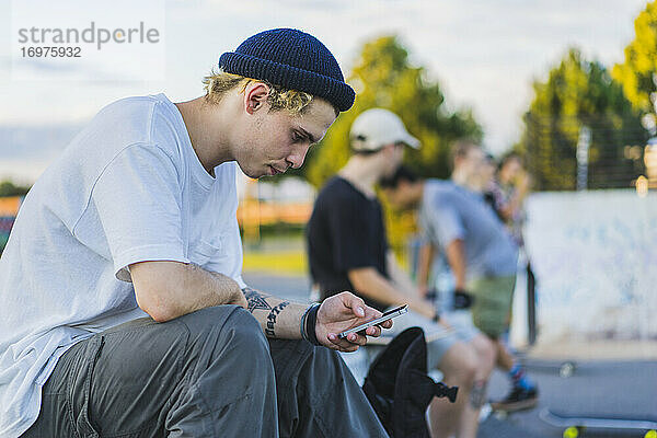 Junger Skater im Skatepark  der sein Smartphone benutzt