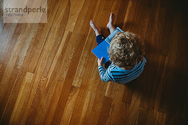 Draufsicht auf ein kleines Kind mit Locken  das auf dem Boden ein Buch liest