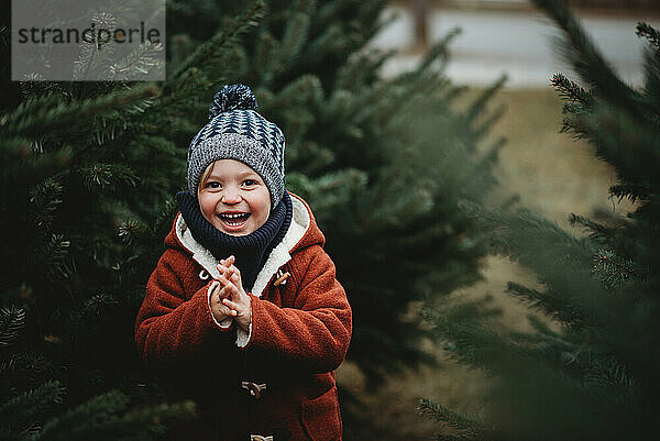 Lächelndes Kind auf einer Baumfarm  das einen Weihnachtsbaum pflückt und Wolle trägt