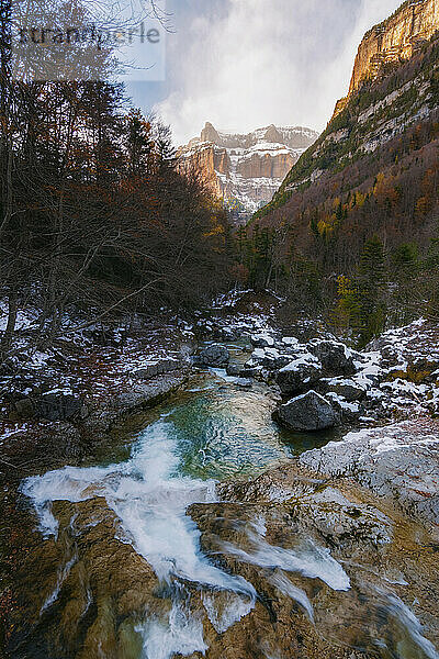 Fluss durch Schneetal mit Wasserfall  Bergen und verschneiten Bäumen