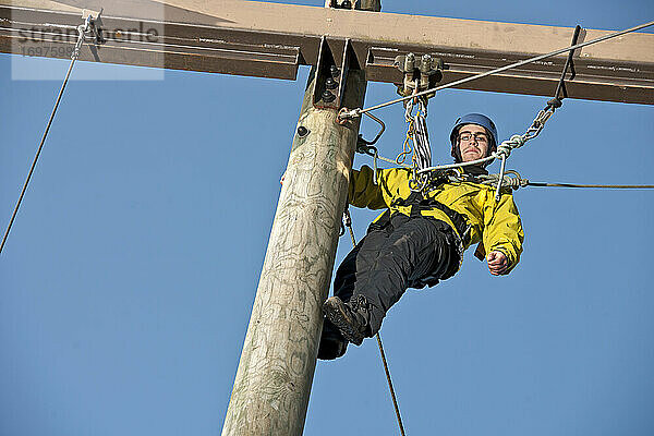 Mann klettert bei einer Hochseilübung auf eine Holzstange