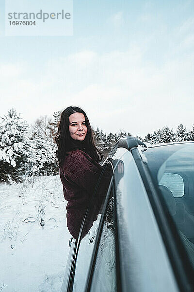 Mädchen posiert auf einer Autotür an einem schönen verschneiten Tag
