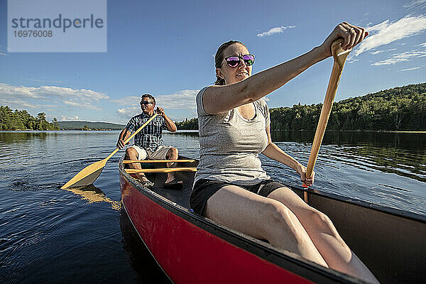 Weiße Frau und schwarzer Mann paddeln mit einem roten Kanu auf einem Waldsee in Maine