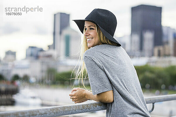 Blonde Frau mit Hut und Stadtsilhouette im Hintergrund