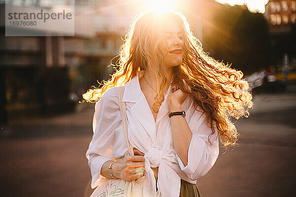 Porträt einer glücklichen erfolgreichen Frau mit zerzaustem Haar in der Stadt bei Sonnenuntergang