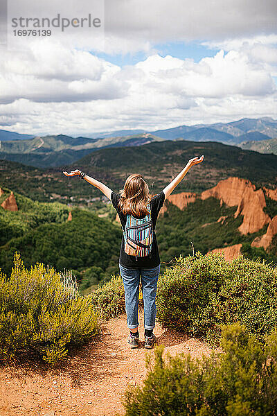 Fröhliche junge Frau mit buntem Rucksack fröhlich in den Bergen