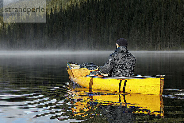 Rückenansicht eines Mannes paddeln Kanu auf ruhigen nebligen See
