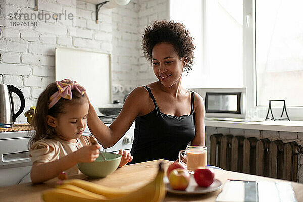 Ethnische Mutter streichelt Tochter beim Frühstück