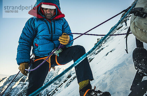Männlicher Kletterer sichert seinen Vorsteiger bei einer kalten alpinen Wintertour