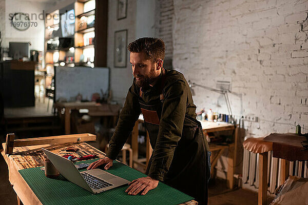 Positiver Kunsthandwerker mit Laptop in der Werkstatt