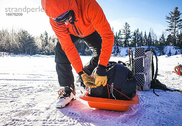 Ein Mann packt auf einem verschneiten Parkplatz einen Pulk-Schlitten zusammen