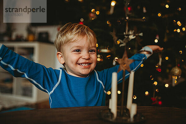 Glücklicher Junge lächelt zu Hause mit einem Weihnachtsbaum im Rücken