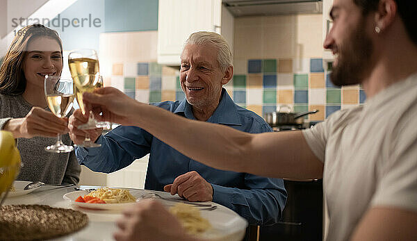 Älterer Mann und junges Paar stoßen beim Familienessen mit Weingläsern an